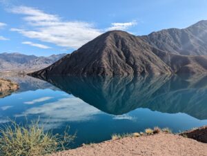 A tranquil lake near Mendoza with crystal-clear water reflecting the rugged mountains and blue sky, creating a picturesque and serene setting.