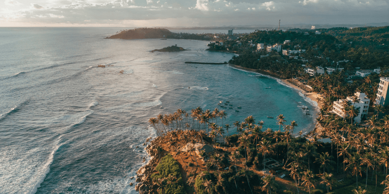 Unwind with this breathtaking view of Sri Lanka’s coastline at sunset, featuring palm trees, turquoise waters, and a tranquil island atmosphere.