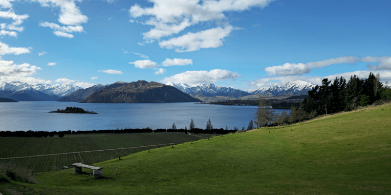 Experience the serene beauty of New Zealand with this stunning view of a pristine lake surrounded by majestic mountains and lush greenery.